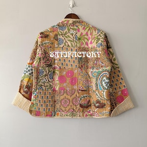 K&ouml;nnte beinhalten: Gesteppte Jacke mit Patchwork-Design mit Blumen- und Paisley-Mustern in Beige-, Rosa-, Blau- und Gr&uuml;nt&ouml;nen. Die Jacke hat einen beige gestreiften Besatz an den Manschetten und am Kragen. Auf der R&uuml;ckseite steht das Wort "SATISFACTORY".