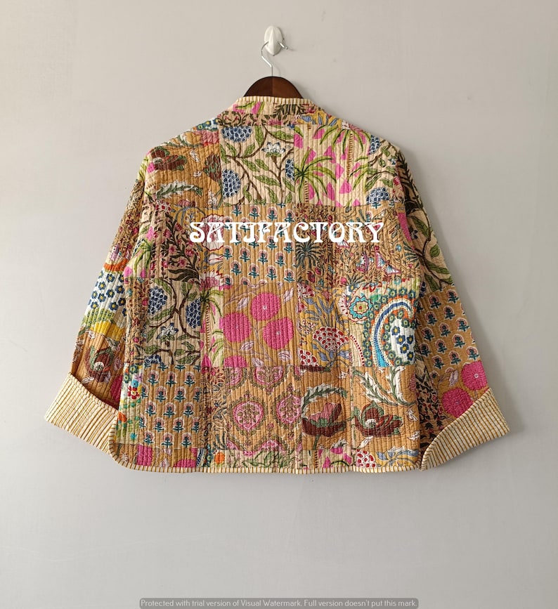 K&ouml;nnte beinhalten: Gesteppte Jacke mit Patchwork-Design mit Blumen- und Paisley-Mustern in Beige-, Rosa-, Blau- und Gr&uuml;nt&ouml;nen. Die Jacke hat einen beige gestreiften Besatz an den Manschetten und am Kragen. Auf der R&uuml;ckseite steht das Wort "SATISFACTORY".
