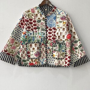 K&ouml;nnte beinhalten: Gesteppte Jacke mit floralem Patchwork-Design. Die Jacke zeigt eine Vielzahl farbenfroher Blumenmuster, darunter rote, blaue und rosa Blumen, auf wei&szlig;em Hintergrund. Die &Auml;rmel und der Saum sind mit schwarz-wei&szlig;en Streifen versehen.