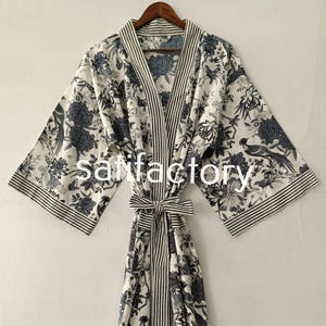 May include: A white robe featuring a dark blue floral and bird pattern with striped trim on the collar, cuffs, and waist tie. The word "satisfactory" is printed in white across the center of the garment, which hangs on a wooden hanger.