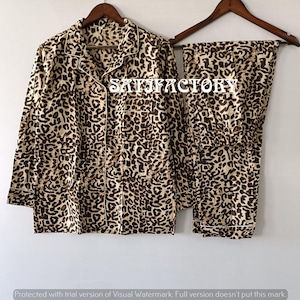 Puede incluir: Conjunto de pijama con estampado de leopardo en tonos marrón y beige. El conjunto incluye una camisa con botones y un pantalón a juego. La camisa tiene un bolsillo en el pecho y ribetes blancos. La palabra "SATISFACTORY" está impresa en la camisa.