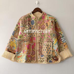 K&ouml;nnte beinhalten: Gesteppte Jacke mit Patchwork-Design mit Blumen- und Paisley-Mustern in Rosa, Gr&uuml;n und Gold. Die Jacke hat einen Stehkragen, zwei Vordertaschen und den Aufdruck "SATISFACTORY" auf der Vorderseite.