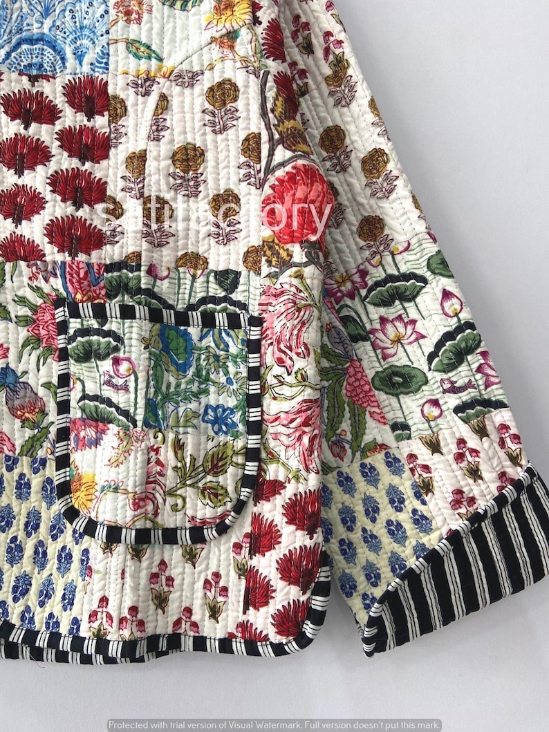 K&ouml;nnte beinhalten: Gesteppte Jacke mit Patchwork-Design mit Blumen- und geometrischen Mustern in Rot, Blau und Gelb auf wei&szlig;em Hintergrund. Die Jacke hat eine schwarz-wei&szlig; gestreifte Bord&uuml;re und eine Tasche.