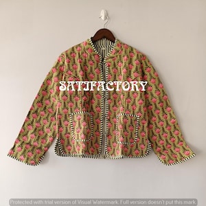 May include: A quilted jacket with a floral pattern in pink and green. The jacket has a black zip, two pockets, and the word "SATIFACTORY" printed on the front. The jacket is hanging on a wooden hanger.