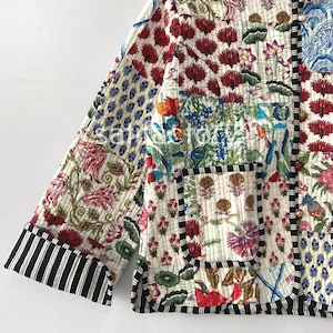 K&ouml;nnte beinhalten: Gesteppte Jacke mit Patchwork-Design mit Blumen- und geometrischen Mustern in Rot, Blau, Gr&uuml;n und Rosa. Die Jacke hat einen schwarz-wei&szlig; gestreiften Besatz an den &Auml;rmeln und Kanten. Die Jacke ist aus einem weichen, gesteppten Stoff gefertigt.