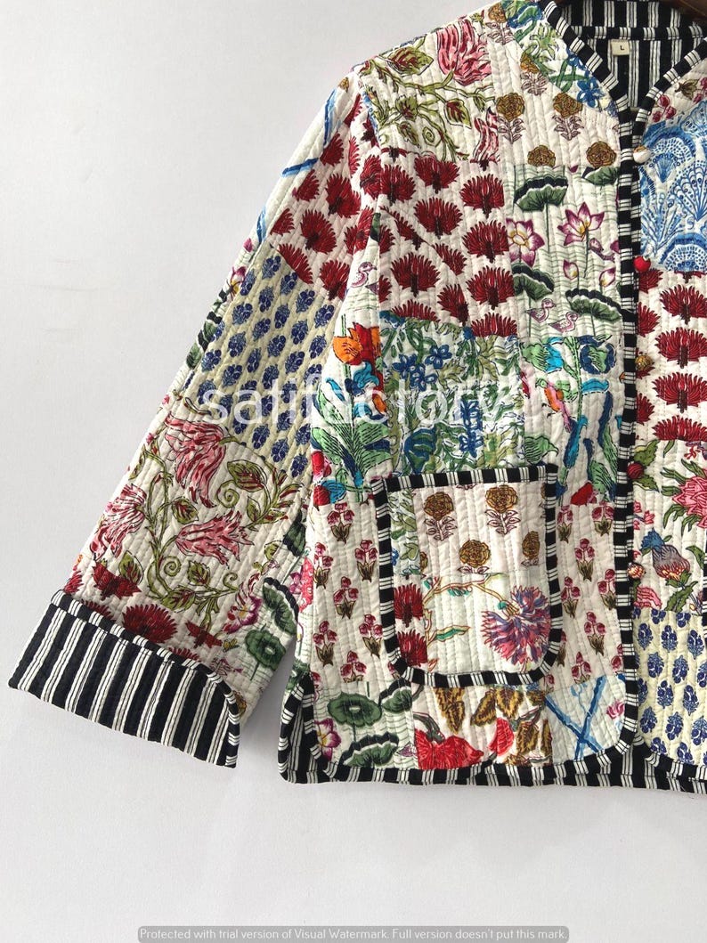 K&ouml;nnte beinhalten: Gesteppte Jacke mit Patchwork-Design mit Blumen- und geometrischen Mustern in Rot, Blau, Gr&uuml;n und Rosa. Die Jacke hat einen schwarz-wei&szlig; gestreiften Besatz an den &Auml;rmeln und Kanten. Die Jacke ist aus einem weichen, gesteppten Stoff gefertigt.
