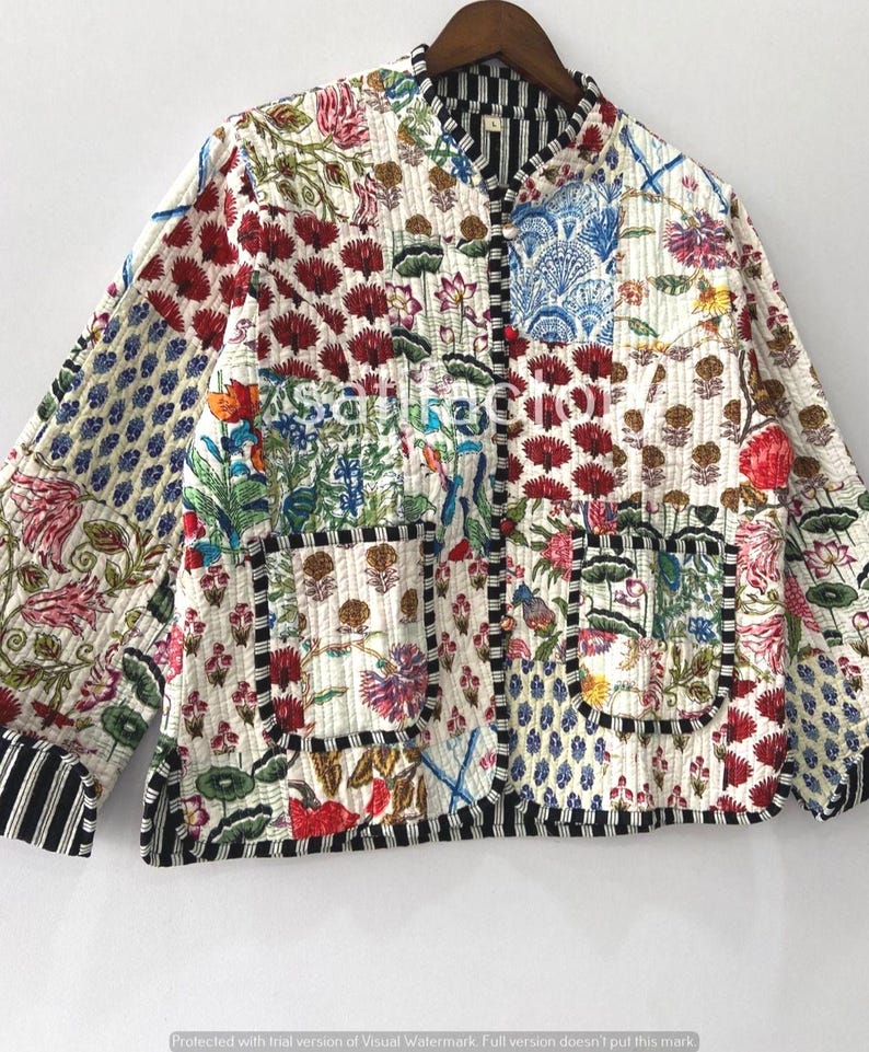 K&ouml;nnte beinhalten: Gesteppte Jacke mit Patchwork-Design mit floralen und geometrischen Mustern in Rot, Blau, Gr&uuml;n und Wei&szlig;. Die Jacke hat eine schwarz-wei&szlig; gestreifte Bord&uuml;re und einen Stehkragen. Die Jacke h&auml;ngt an einem Holzkleiderb&uuml;gel.