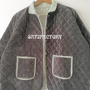 以下が含まれることがあります： ダークグレーのリバーシブルキルトジャケット。ダイヤモンド柄で、ストライプの裏地とトリム、フロントポケット2つ、ボタン留めが特徴です。「SATISFACTORY」の文字がプリントされています。