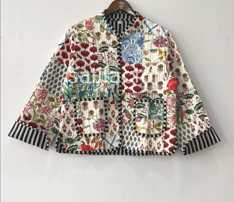 K&ouml;nnte beinhalten: Gesteppte Jacke mit Patchwork-Design. Sie zeigt Blumen- und geometrische Muster in Rot, Blau, Gr&uuml;n und Wei&szlig;. Die Jacke hat einen Stehkragen, zwei Taschen und schwarz-wei&szlig; gestreifte Manschetten und Bes&auml;tze.