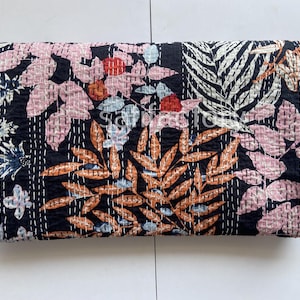 Pode incluir: Um edredom preto dobrado com um padrão floral. O edredom apresenta flores e folhas rosa, laranja e brancas, costuradas com fio branco. O design geral é uma mistura de elementos botânicos.