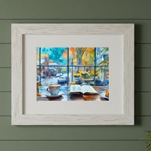 May include: A framed watercolor print featuring a view through a window of a street scene with a coffee cup and an open book on a table in the foreground. The artwork is encased in a white wooden frame with a white mat board border.