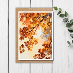 May include: A watercolor painting of autumn leaves in shades of orange and yellow, with a view looking up through the branches. The artwork is set against a soft, light background and is presented in a brown card.