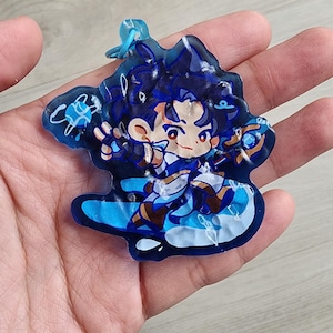 May include: A translucent blue acrylic keyring featuring a stylised anime character with dark hair, wearing a white and blue outfit, holding a staff, and surrounded by swirling blue energy effects, attached to a small blue plastic ring connector.