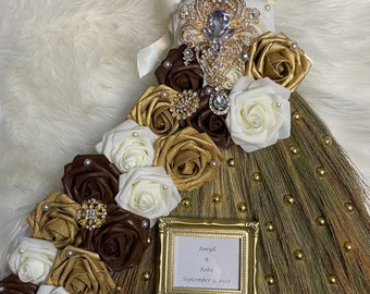 Peut inclure: Un balai brun et doré décoré de roses blanches et brunes, de ruban doré et de broches ornées de bijoux. Un petit cadre doré avec le texte "Jimyll & Reba September 3, 2022" est fixé au balai.