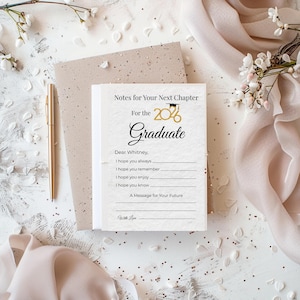 Könnte beinhalten: Ein Schreibwarenset zum Thema Abschluss, das einen Stapel weißer Notizkarten mit dem Text "Notes for Your Next Chapter" und "Graduate" zeigt. Ein goldener Stift und ein dekorativer Umschlag sind ebenfalls vorhanden. Der Hintergrund umfasst florale Akzente.