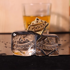 May include: Two clear ice cubes with a gold mountain design and the word "Bernice" embossed on each. A gold mountain design with the word "Bernice" is on top of the ice cubes.