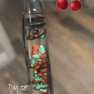 Op de afbeelding: Een transparante pen met rode glitter en oranje en groene vormen erin. De pen heeft een zilveren bovenkant en een witte onderkant. De tekst "DM to order" en "Cherry pen available" staat op de afbeelding.