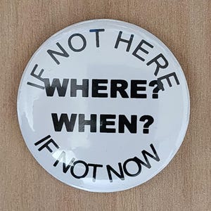 May include: A white button with black text. The text reads "IF NOT HERE WHERE? WHEN? IF NOT NOW" in a circular arrangement. The button is round and appears to be made of metal or plastic.