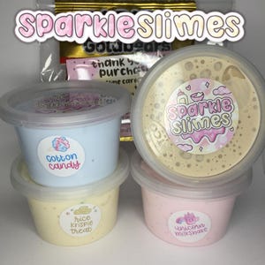 Puede incluir: Cuatro recipientes de Sparkle Slimes, cada uno lleno de slime colorido. Los recipientes están etiquetados como "Cotton Candy", "Rice Krispie Treat" y "Unicorn Milkshake". El recipiente superior tiene el logotipo de Sparkle Slimes.