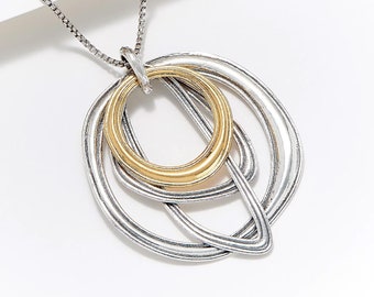 May include: Silver-toned necklace with a pendant featuring overlapping rings. The central ring is gold-colored, while the other rings are silver. The necklace has a delicate chain and is displayed against a white background.