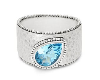 Puede incluir: Un anillo de plata con una banda texturizada y una piedra preciosa de topacio azul en forma de lágrima.