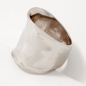 Puede incluir: Un anillo de plata con una banda ancha, lisa y ligeramente curvada.