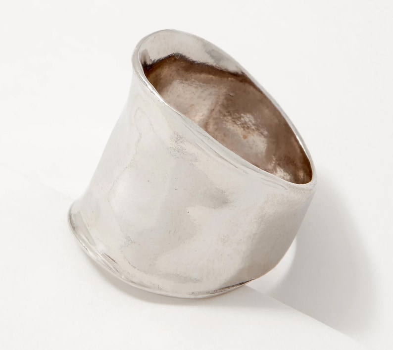 Puede incluir: Un anillo de plata con una banda ancha, lisa y ligeramente curvada.