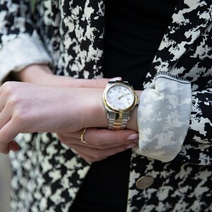 May include: A silver and gold wristwatch with a white face and black hands. The watch is on a person's wrist.
