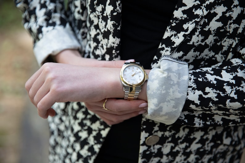 May include: A silver and gold wristwatch with a white face and black hands. The watch is on a person's wrist.