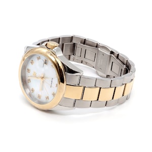May include: A two-tone silver and gold wristwatch with a white face and diamond accents. The watch has a stainless steel band and a quartz movement.
