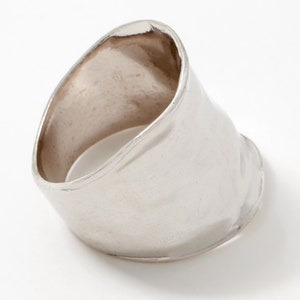 Puede incluir: Un anillo de plata con una banda ancha y lisa que est&aacute; ligeramente curvada. El anillo est&aacute; hecho de metal y tiene un acabado pulido.