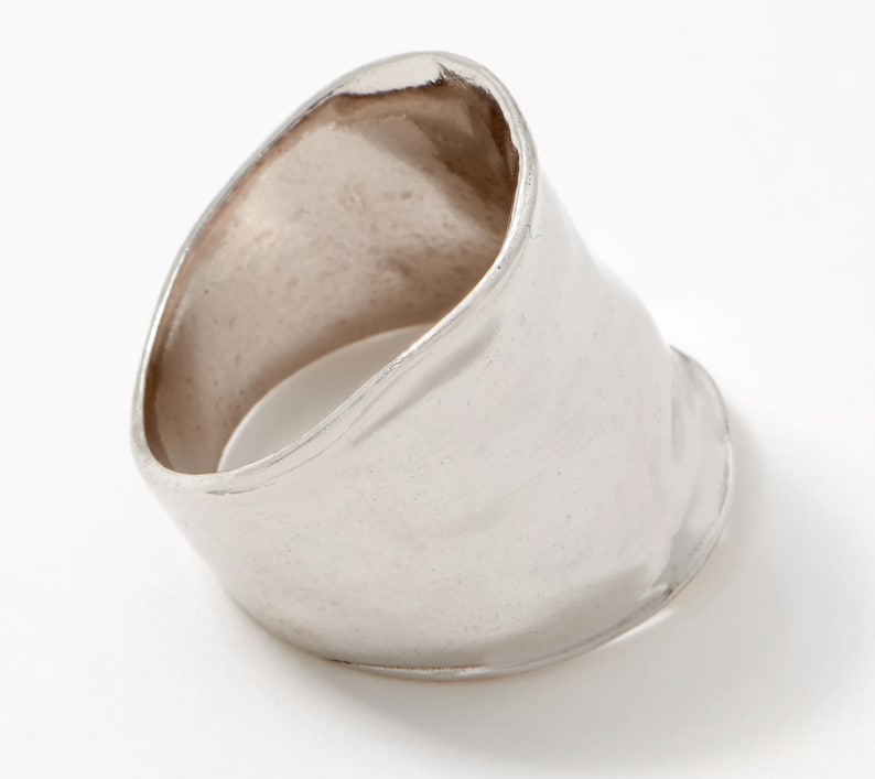 Puede incluir: Un anillo de plata con una banda ancha y lisa que est&aacute; ligeramente curvada. El anillo est&aacute; hecho de metal y tiene un acabado pulido.