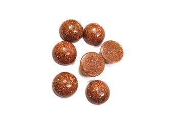 May include: Seven round, brown, gemstone cabochons with a speckled texture. The cabochons are scattered on a white surface.