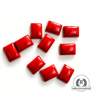 May include: Ten red rectangular gemstone cabochons, scattered on a white surface.