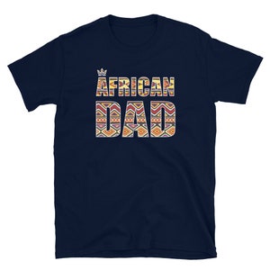 May include: Navy blue t-shirt with the words "AFRICAN DAD" in a colorful, patterned design. A small crown graphic is above the word "AFRICAN". The shirt is made of a soft material.