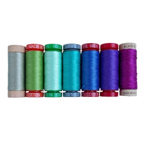 May include: Eight spools of Aurifil thread in various shades of blue, green, and purple. The spools are labeled "Aurifil" and "Made in Italy".