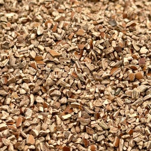 May include: Close-up of a pile of small, irregularly shaped pieces. The pieces are primarily light brown with darker brown and tan accents, creating a textured, natural appearance. The overall effect suggests a raw, organic material.