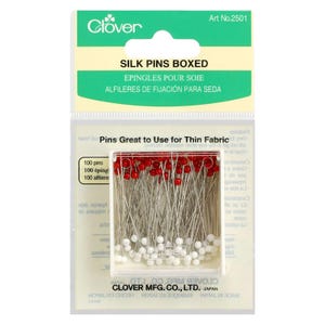 May include: Boxed silk pins with red and white heads, ideal for sewing. The package includes 100 pins, perfect for delicate fabrics. The packaging features the Clover brand logo and text in multiple languages.