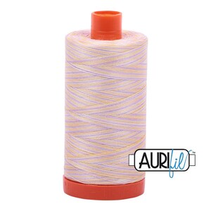 May include: A spool of sewing thread featuring a variegated pattern of light purple and soft yellow fibers wound around a cylindrical core. The spool has a bright orange plastic cap at the top and a matching orange base, with the Aurifil logo printed.