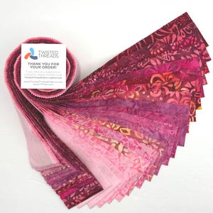 May include: A jelly roll of fabric strips in various shades of pink, magenta, and deep red, featuring batik-style patterns. A white square card is attached to the roll with the text Twisted Threads, Thank You For Your Order, and contact details.