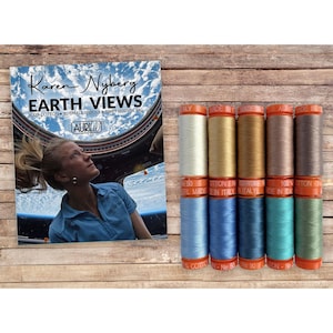 May include: A set of ten small spools of 50wt cotton thread in various colors, arranged in two rows of five. Next to the spools is a product box labeled Karen Nyberg Earth Views, featuring an image of a person looking out a window at Earth.