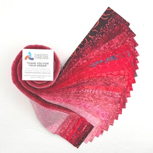May include: A jelly roll of fabric strips featuring a gradient of pink and red hues with various batik patterns. A square white card is attached to the roll, displaying the text Twisted Threads, Thank You For Your Order, and contact details.