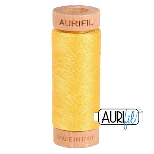 May include: A spool of bright yellow sewing thread wound around a light-colored wooden core. The top of the wooden spool is embossed with the text AURIFIL, and the bottom is embossed with the text MADE IN ITALY. The thread is smooth and uniform.