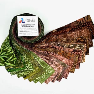 May include: A jelly roll of fabric strips featuring batik patterns in a gradient of green, brown, and tan shades. A white square card is placed on top with the text Twisted Threads, Thank You For Your Order, and contact information.