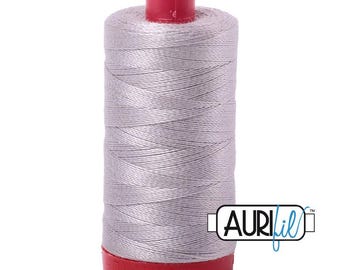 Puede incluir: Un carrete de hilo de coser gris claro enrollado alrededor de un núcleo cilíndrico con una parte superior y una base de plástico rojo brillante. La marca AURIfil está impresa en texto negro y azul en una etiqueta blanca en el lateral.