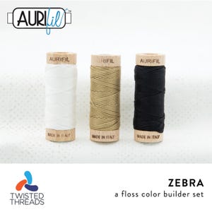 May include: Three wooden spools of Aurifil floss in white, tan, and black. Each spool is branded with Aurifil and Made in Italy. The set is labeled Zebra a floss color builder set by Twisted Threads. The top features the Aurifil logo.