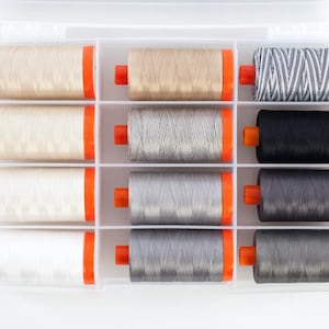 Op de afbeelding: Een transparante kunststof opbergdoos met 12 spoelen garen. De spoelen zijn gerangschikt in drie rijen van vier. De spoelen zijn in tinten beige, grijs en zwart.