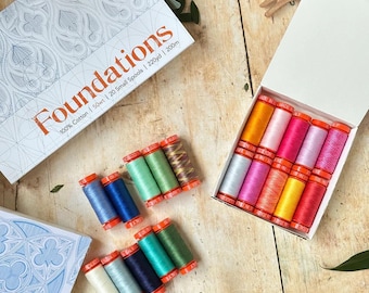 Puede incluir: Un juego de bobinas de hilo 100% algodón Foundations, 50wt, 20 bobinas pequeñas, 220yd, 200m. La colección incluye una caja blanca con un patrón geométrico azul y una caja abierta con diez bobinas de colores, con diez bobinas adicionales fuera.