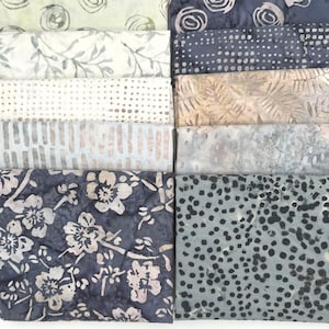 May include: A collection of folded fabric squares in various patterns and colors. Designs include floral, dotted, and swirling motifs in shades of blue, gray, and cream. The fabrics appear to be cotton or a similar material, suitable for quilting or crafting projects.