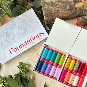 May include: A set of 20 small spools of 100% cotton thread in a white box labeled Foundations. The box contains various colors including blue, green, yellow, pink, and red. Each spool contains 54 yards of 12wt thread. The box lid features a gray pattern.
